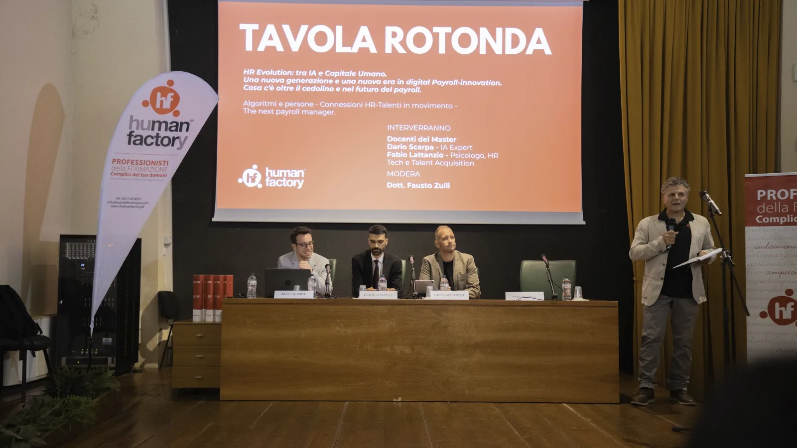 Tavola rotonda del master paghe e contributi di Human Factory sull’IA nel payroll: tre relatori al tavolo e Fausto Zulli che modera in piedi al microfono